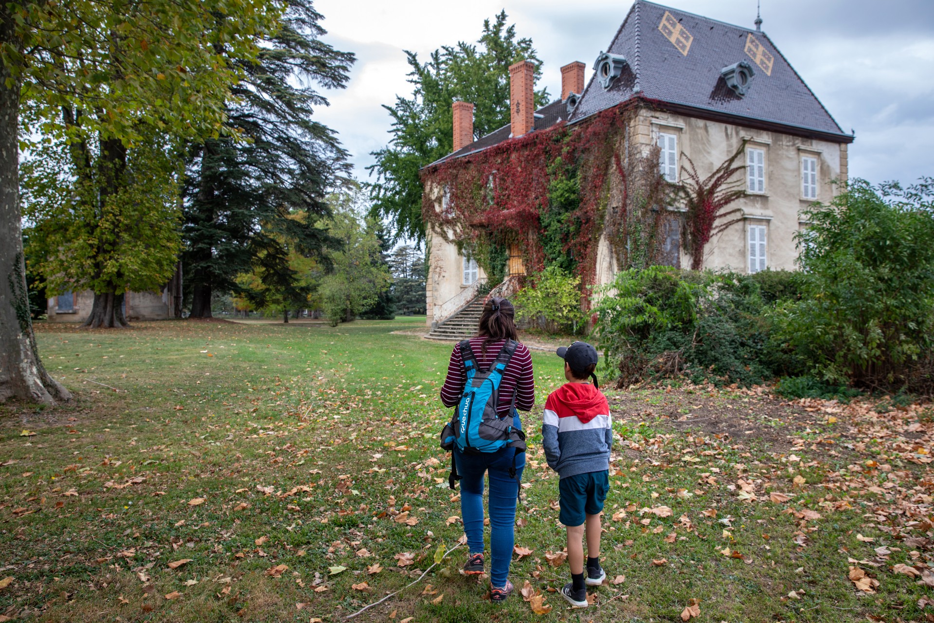 Une mère et son fils de dos au premier plan, dans un jardin à Chaponnay jouant au Gnolus. Une bâtisse est en deuxième plan.