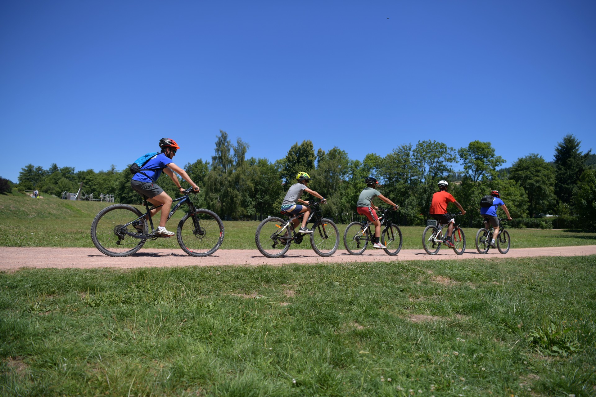 4 enfants font du VTT avec un adulte. Il sont sur un chemin plat qui circule entre des pelouses