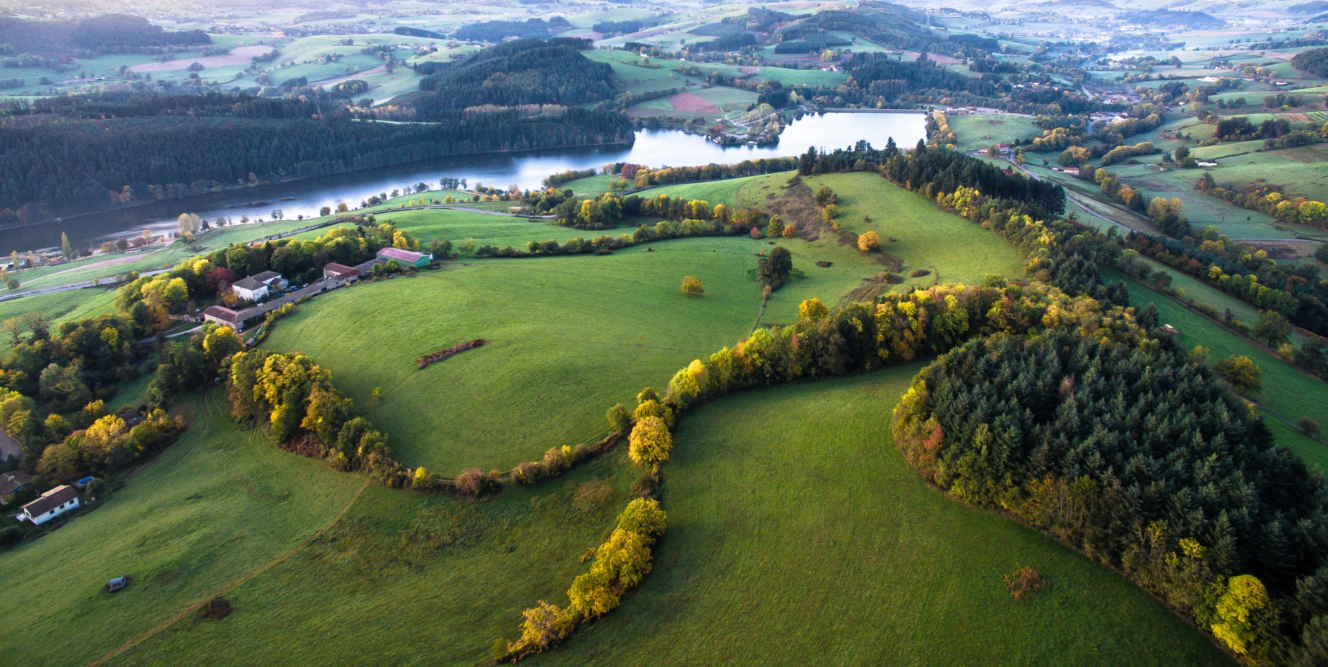 Le lac des Sapins vu du ciel à l'automne dans le Beaujolais Vert. Le 1er plan est occupé par des collines boisées et bocagères.
