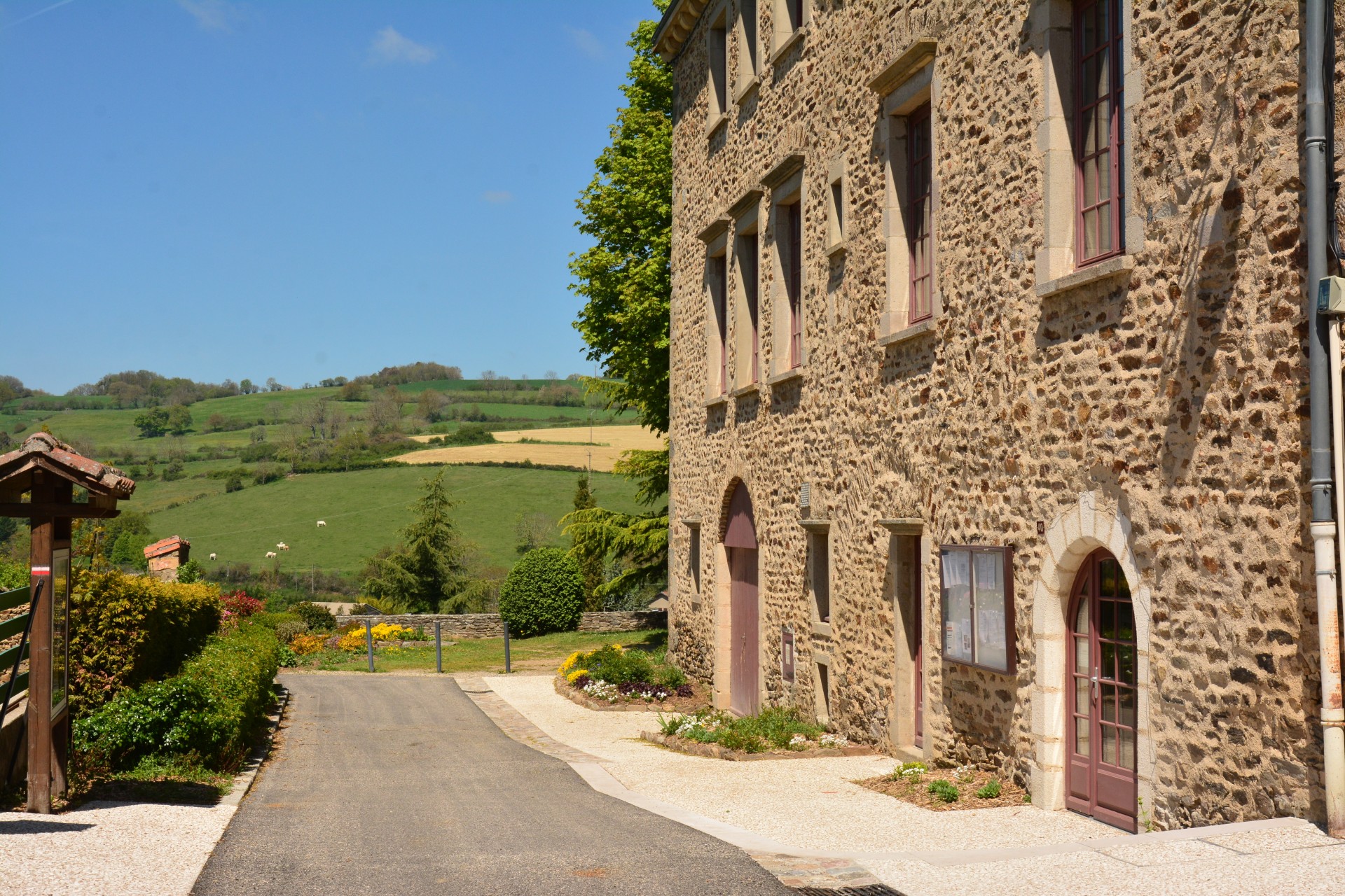Belle bâtisse en pierre où se situe la mairie de Riverie sur la droite et vue sur les Monts du Lyonnais en face.