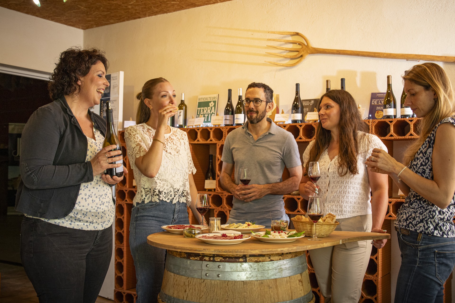 4 femmes et un homme font une dégustation de vin du Beaujolais, accompagnée d'un mâchon. ILs sont dans un caveau autour d'un tonneau sur lequel est posé le repas.