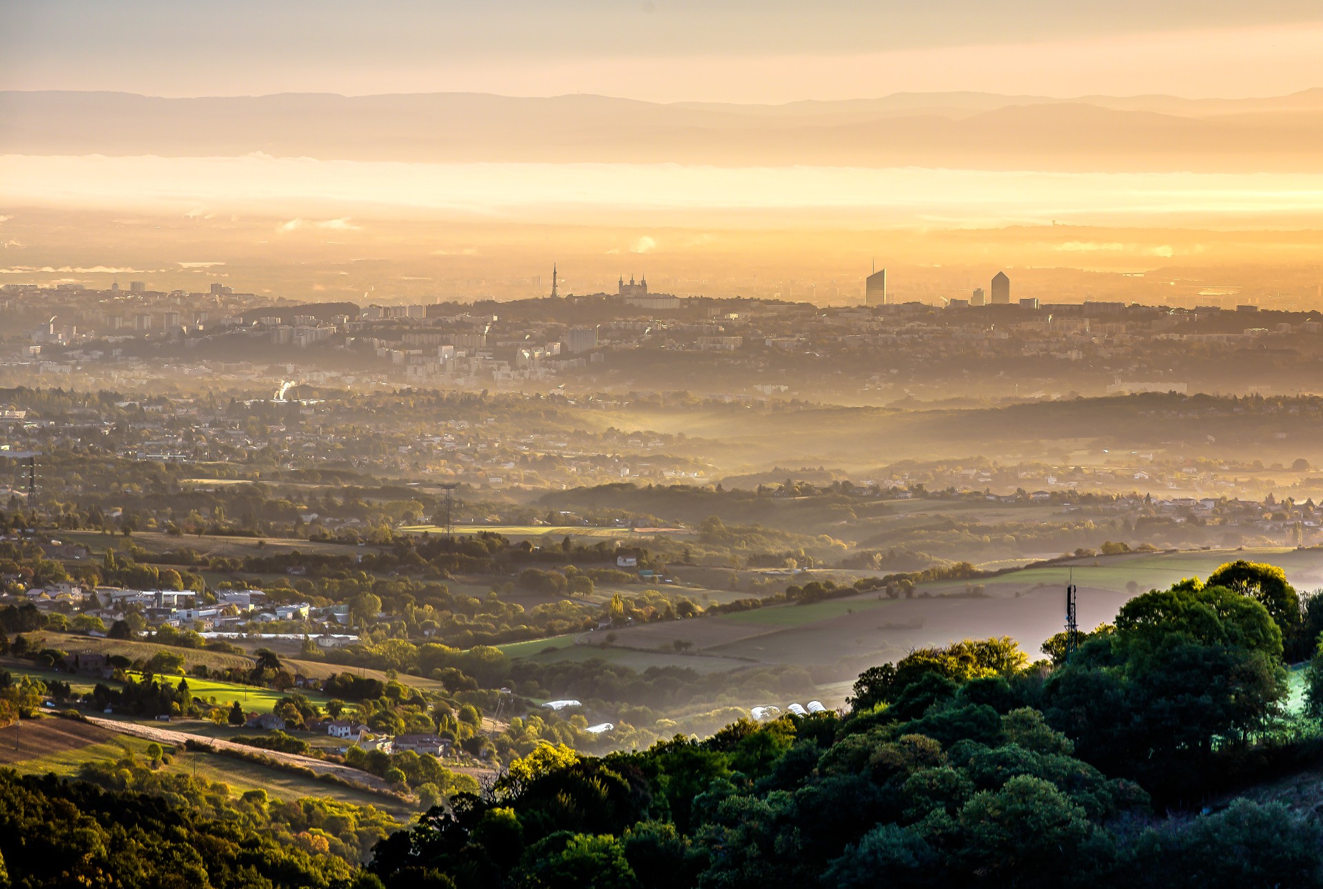 Vue sur Lyon depuis Yzeron. Zoom sur la colline de Fourvière et la tour de la Part Dieu avec au premier plan, les premières collines des Monts du Lyonnais. Levé de soleil avec la brume qui se lève.