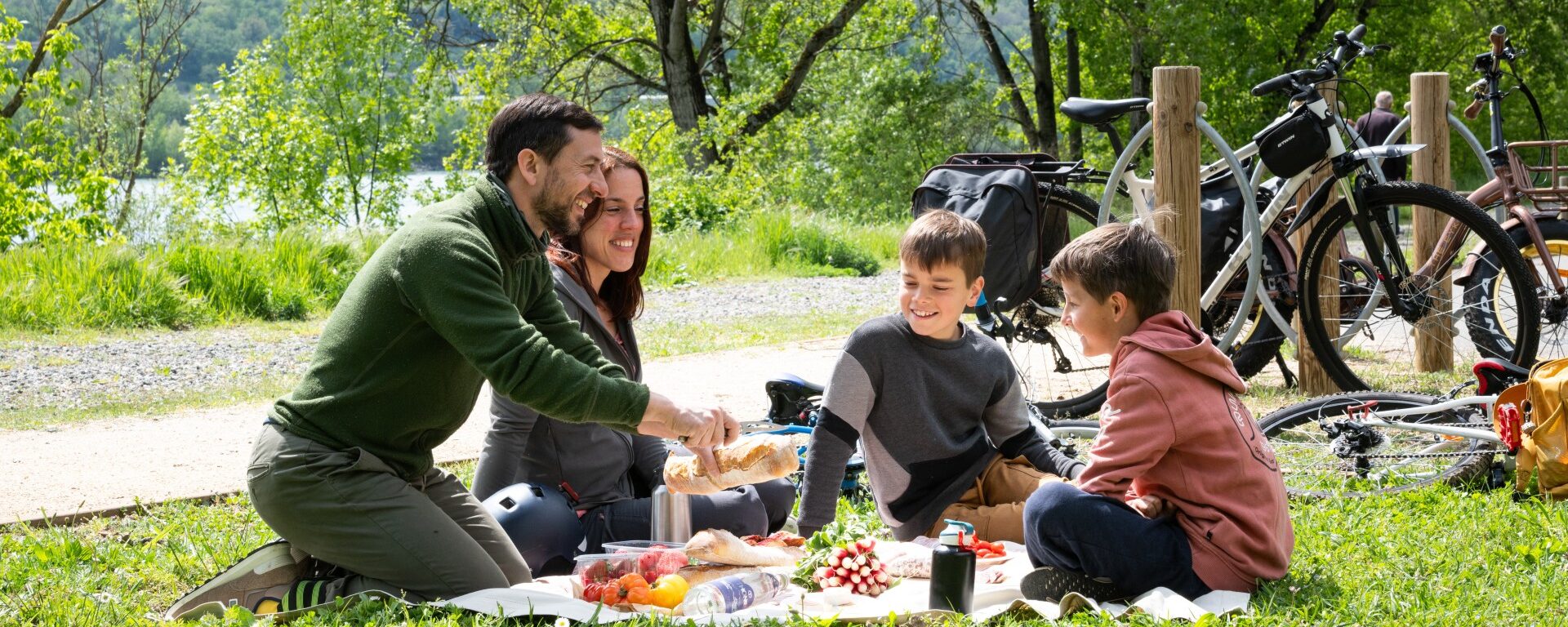 Couple avec enfants au premier plan en pause pique-nique lors d'une balade à vélo sur la ViaRhôna à Ampuis