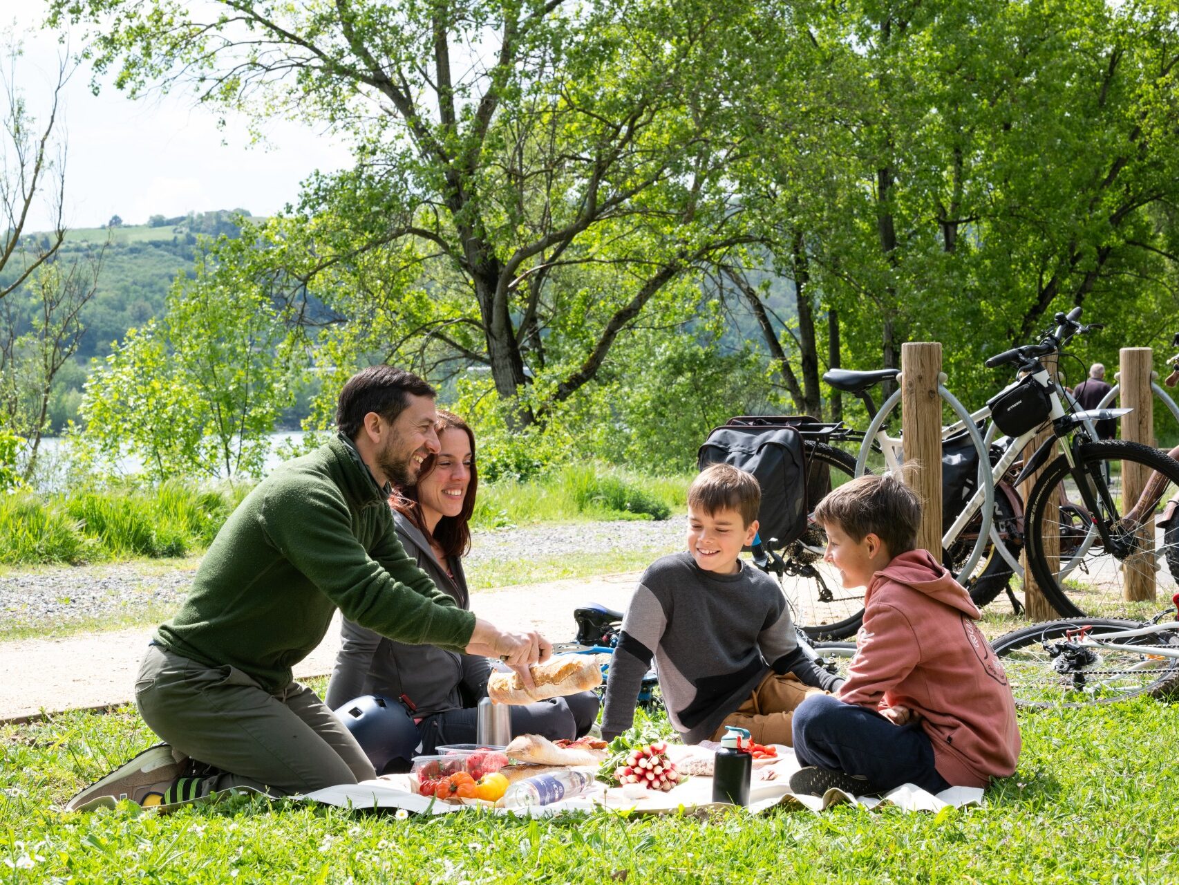 Couple avec enfants au premier plan en pause pique-nique lors d'une balade à vélo sur la ViaRhôna à Ampuis