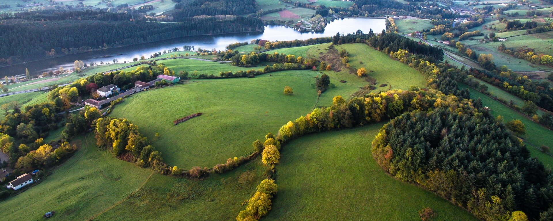Le lac des Sapins vu du ciel à l'automne dans le Beaujolais Vert. Le 1er plan est occupé par des collines boisées et bocagères.