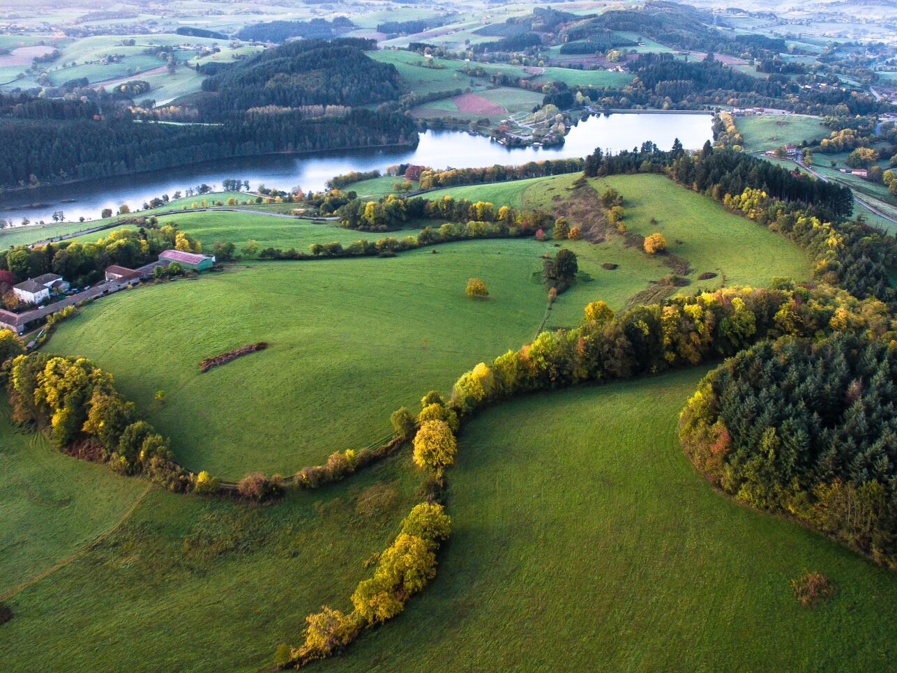 Le lac des Sapins vu du ciel à l'automne dans le Beaujolais Vert. Le 1er plan est occupé par des collines boisées et bocagères.