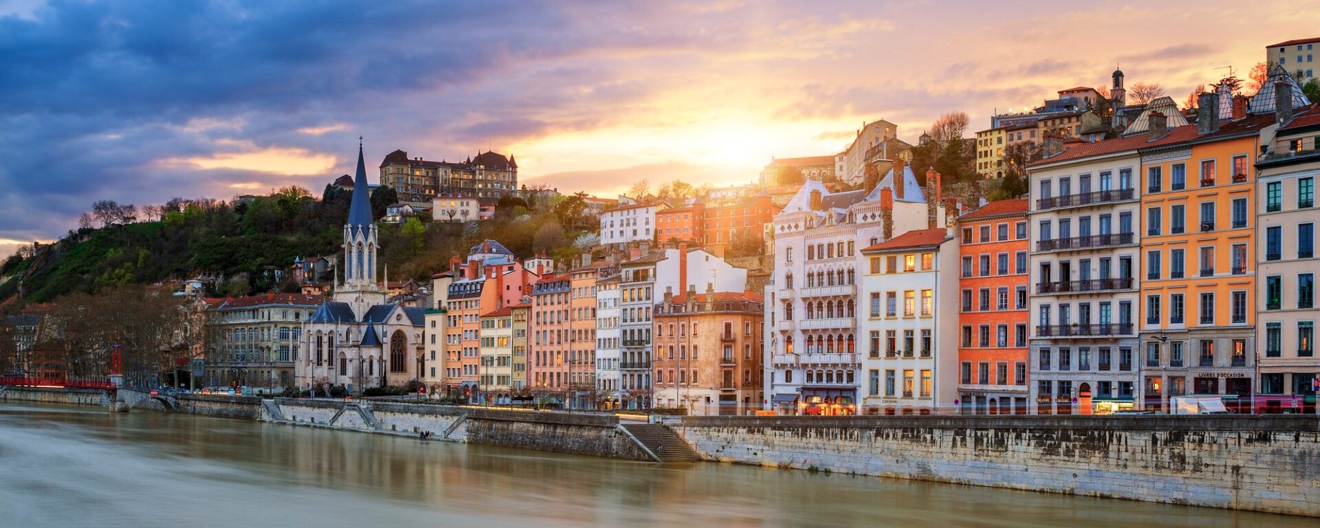 Une vue sur la Saône en premier plan et au loin bâtiments d'époque et l'église saint-Georges de Lyon au coucher de soleil.