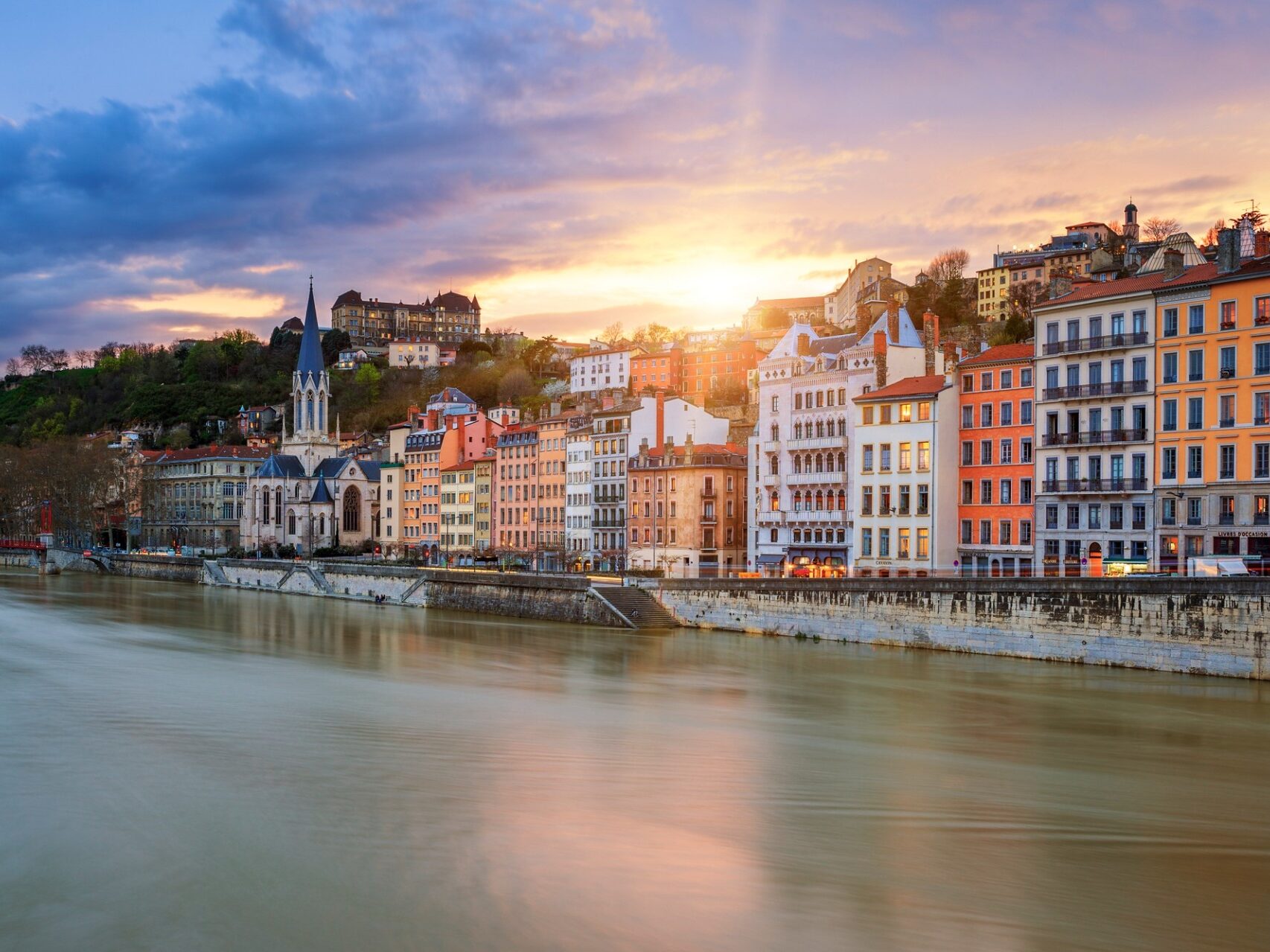 Une vue sur la Saône en premier plan et au loin bâtiments d'époque et l'église saint-Georges de Lyon au coucher de soleil.