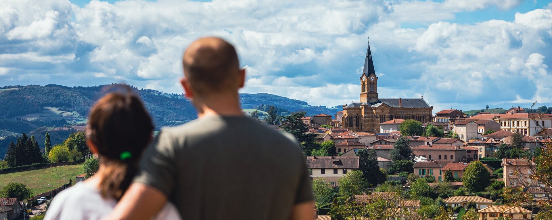 Un couple de dos qui regarde le village de Bessenay. Vue sur son église et les Monts du Lyonnais.